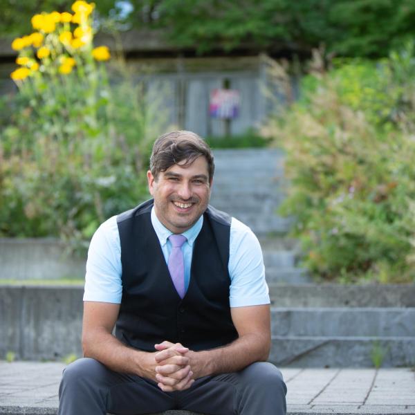 Michael MacKenzie, man with short brown hair, is sitting outside in front of garden and treed area