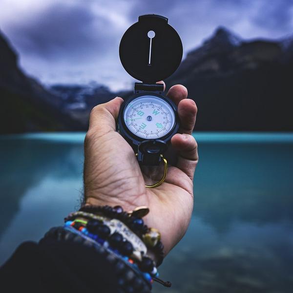 Hand holding a compass with a lake and mountains in the background