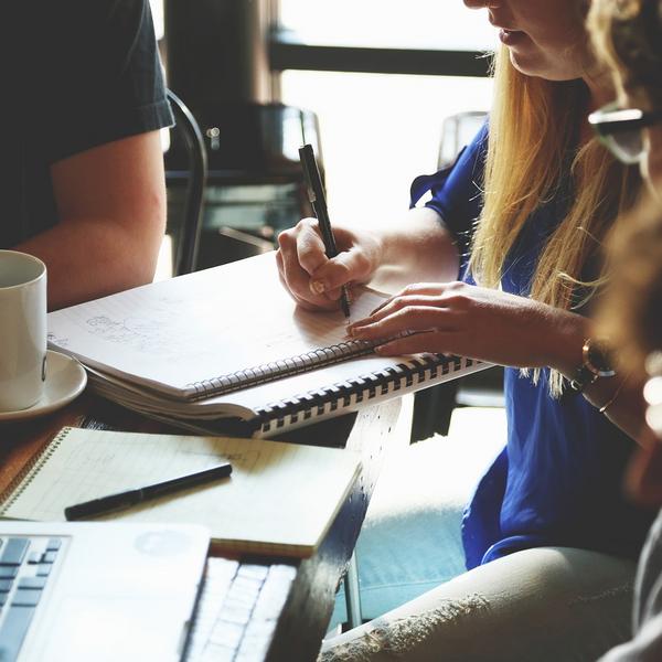 People sitting around a table with a notebook, computer and coffee mug