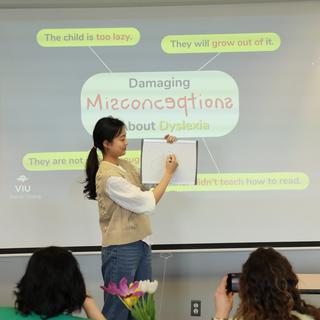 Student writing on a piece of paper in front of a screen with presentation.