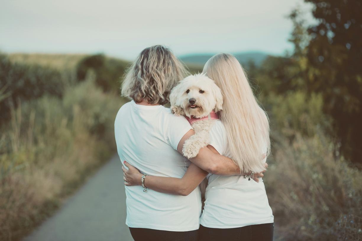 Back of two people wearing white shirts and hugging a white dog